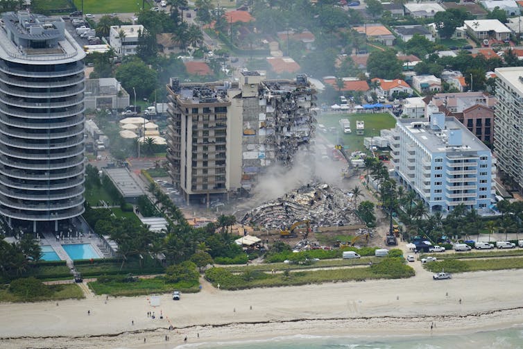 An aerial photo of four condo towers on the beach. In the center is Champlain Towers South, which partially collapsed in June 2021.