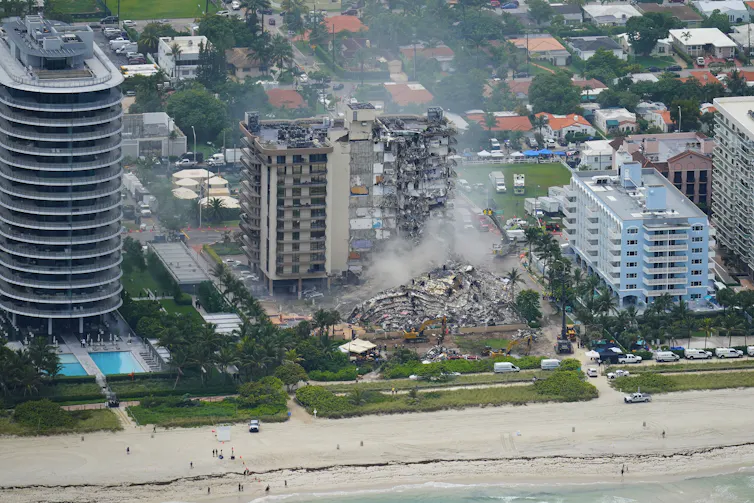 An aerial photo of four condo towers on the beach. In the center is Champlain Towers South, which partially collapsed in June 2021.