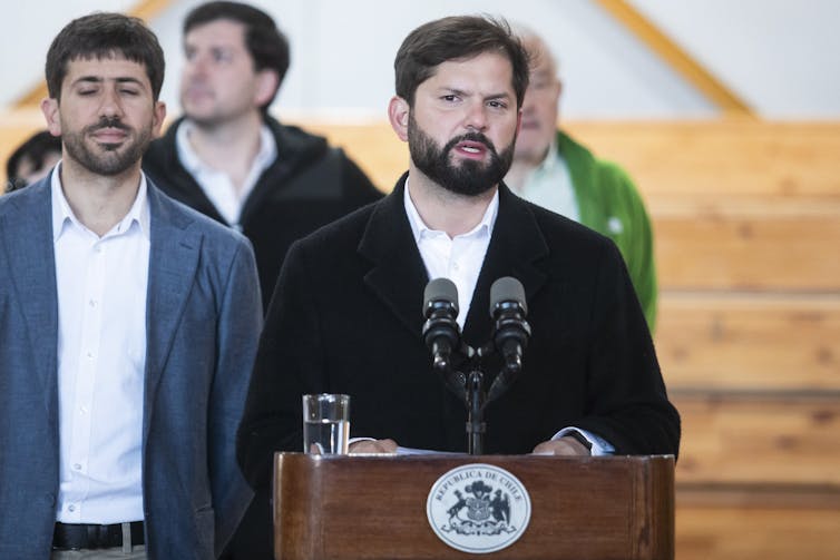 A man with a black beard speaking at a podium