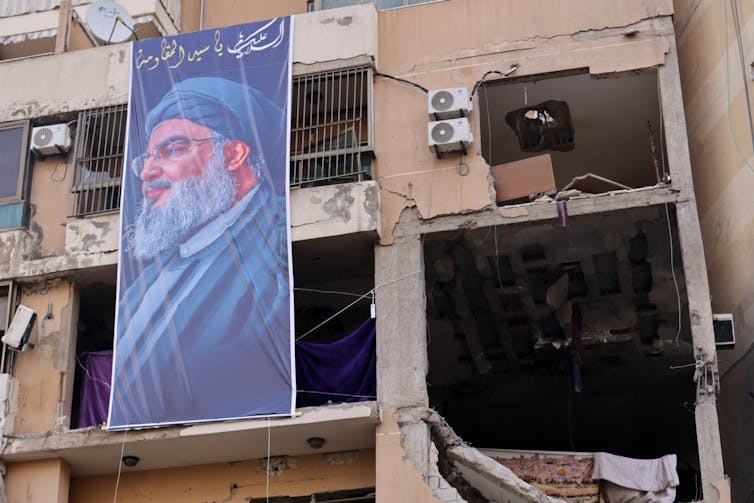 A poster of a man with a beard hangs outside a destroyed building.