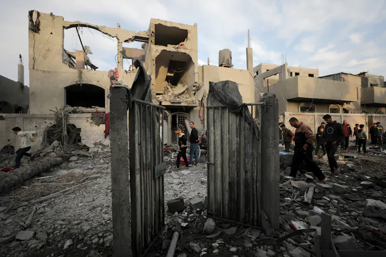 The concrete rubble of a bombed building, with a small group of people inspecting it
