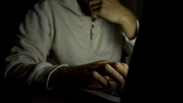 A person sits in a dark room looking at a computer