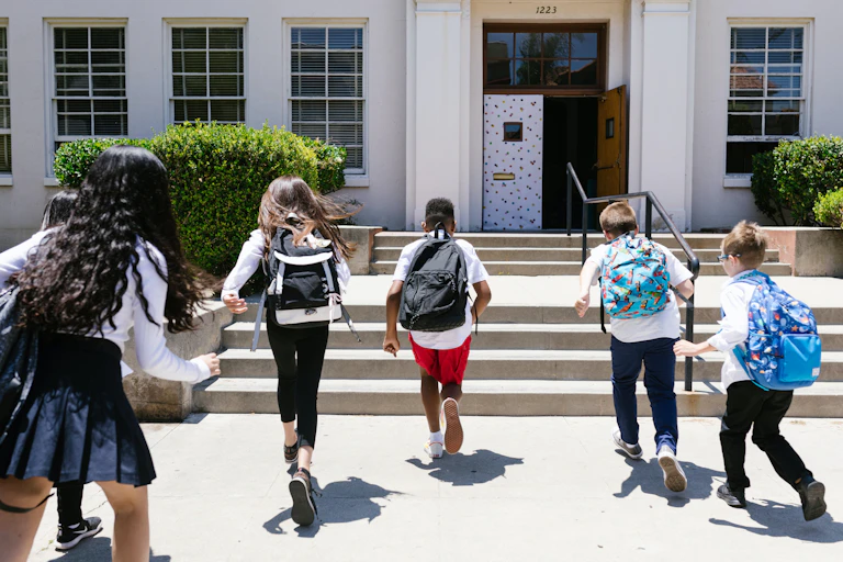 Six school students, wearing back packs run into a school building.