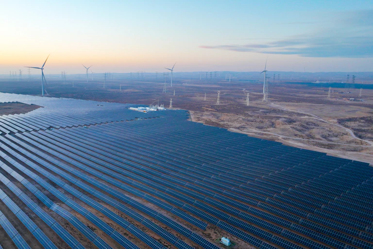 Aerial view of large area of solar panels and wind turbines.