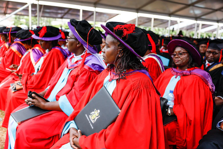 Seated people wearing red robes and black caps with purple brims and purple hoods over their shoulders.
