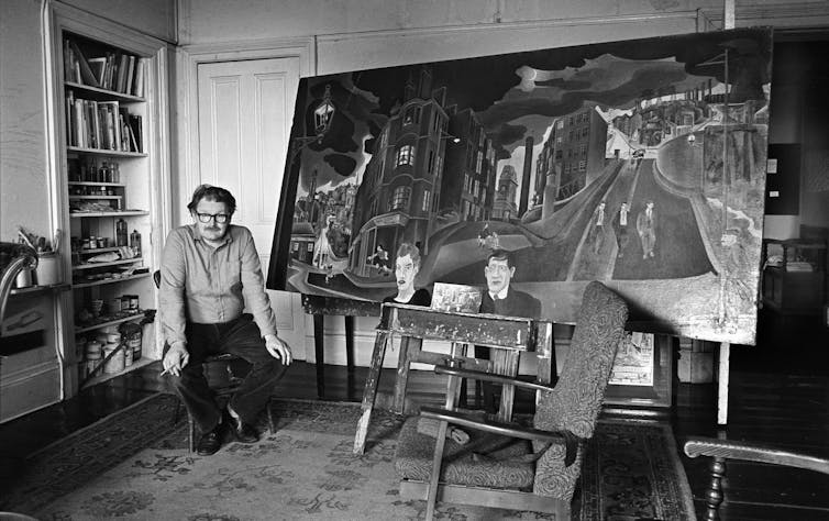 Alasdair Gray sentado junto a uno de sus cuadros en Glasgow, 1983.