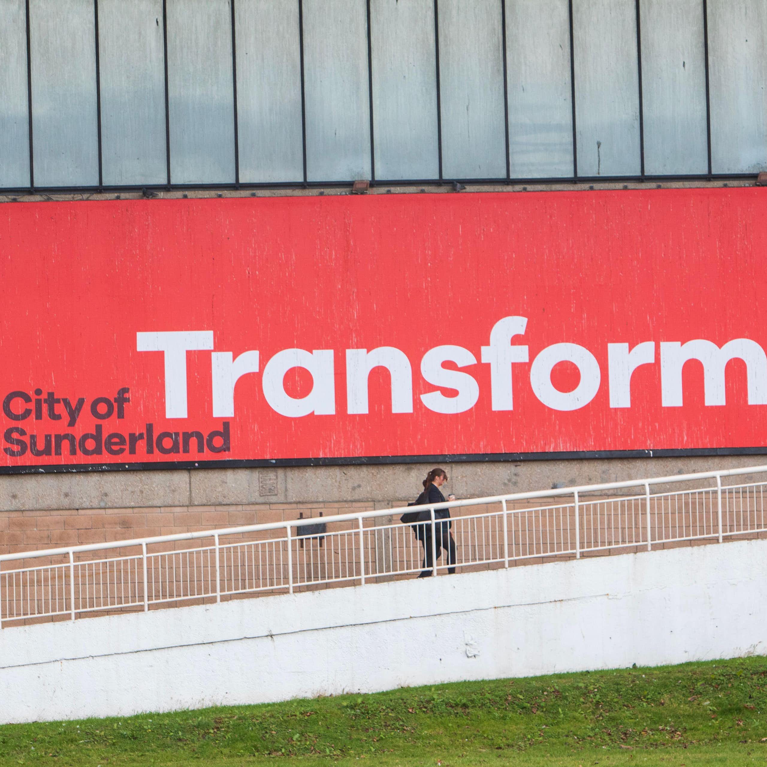 Person walking up stairs in front of a large advert for the city of Sunderland.