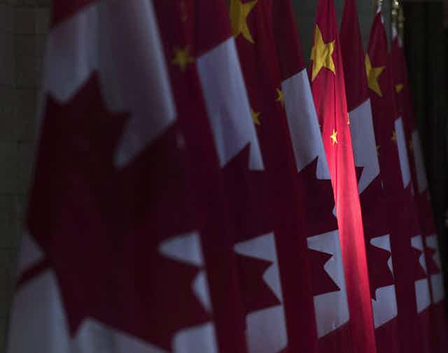 A red and yellow Chinese flag is illuminated in a row of Canadian flags.