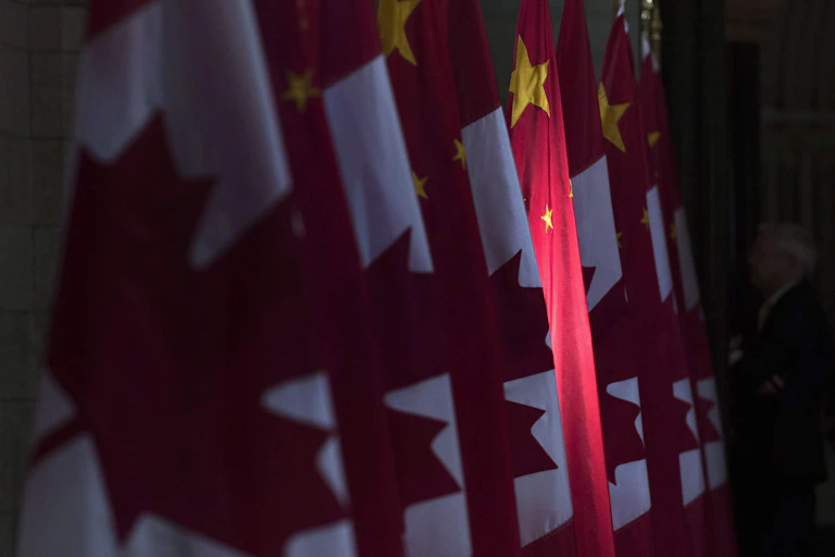 A red and yellow Chinese flag is illuminated in a row of Canadian flags.