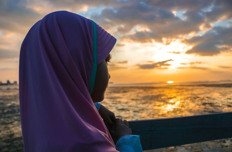 A young girl in a pink hijab watches a sunset