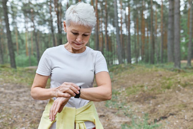 A female runner in the bush looking at a watch.