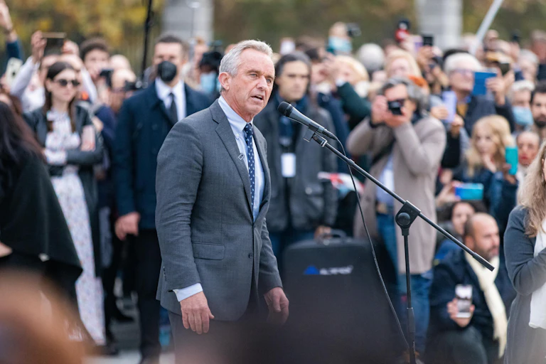 Robert F Kennedy Jr wearing a suit stands at a microphone.