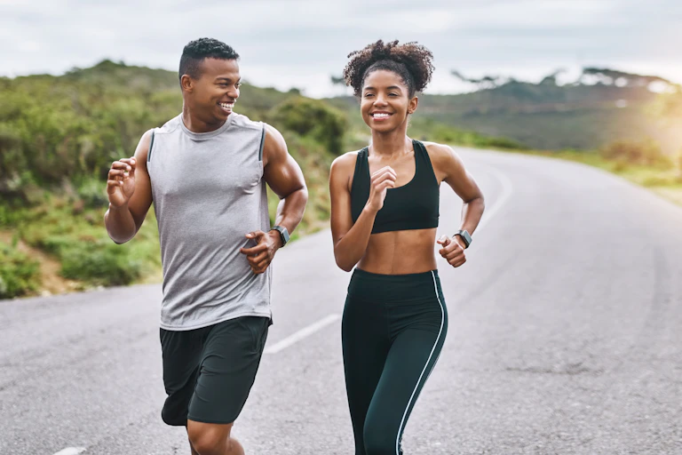 A smiling young man and woman run along a road.