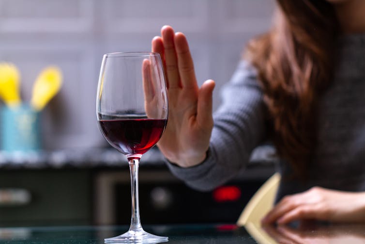 A woman holds up her hand at a glass of red wine to say no.