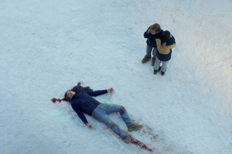 A still from Anatomy of a Fall featuring the husband dead and the wife and son watching on.