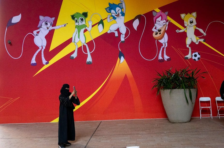 Une femme prend des photos devant une bannière affichant les mascottes officielles de la Coupe d'Asie à Doha.