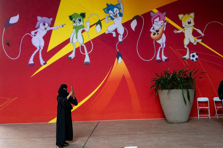 Une femme prend des photos devant une bannière affichant les mascottes officielles de la Coupe d'Asie à Doha.