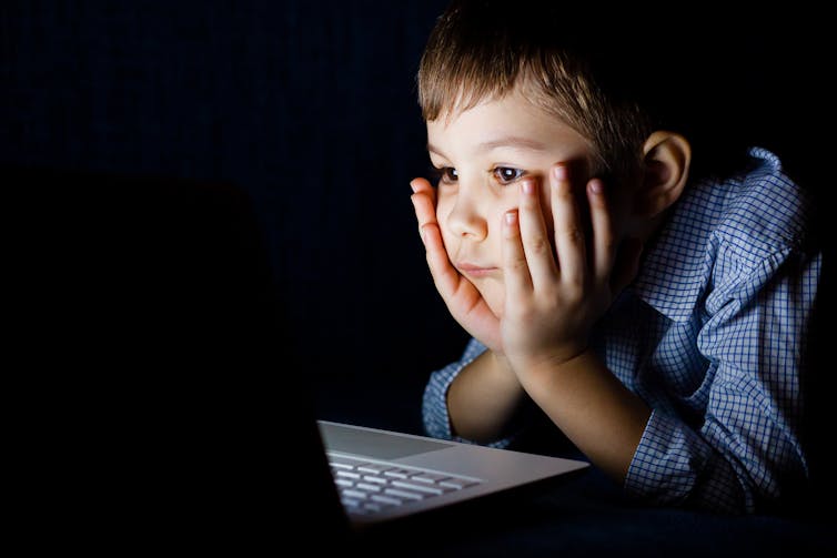 a young boy stares at a laptop screen in the dark