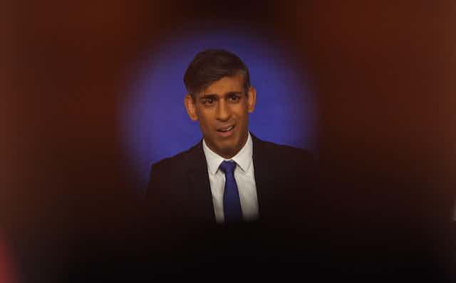 Rishi Sunak seen through a camera lens, flanked by union flags. 