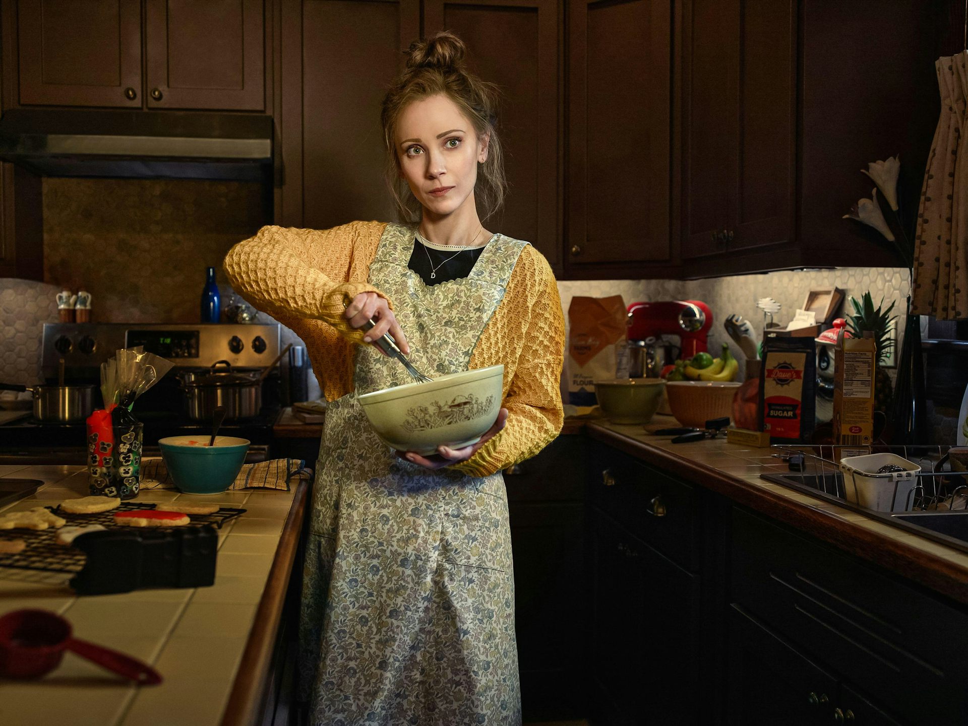 Juno Temple in a kitchen stirring a mixing bowl.