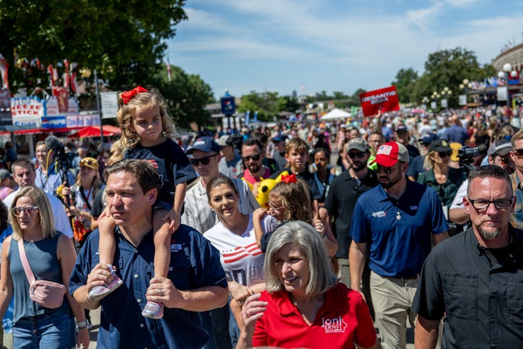 A white man carres his daughter on his shoulders as he walks with hundreds of other white people.