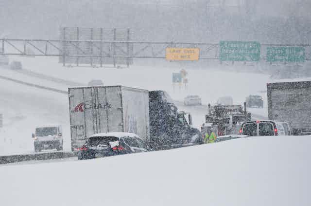 Trucks and other vehicles are backed up on a highway in the snow.