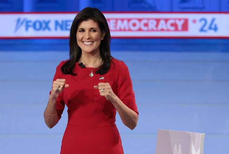 A woman wearing a red dress holda a microphone in front of a sign that says Fox News Democracy '24.