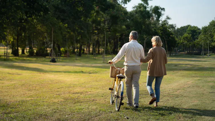 An elderly couple walking in a park with a bicycle