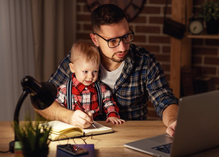 A man with a young child in his lap working on a laptop.