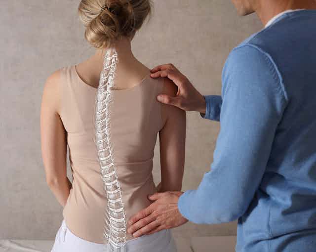 A woman with Scoliosis is examined by a doctor wearing a blue jacket.