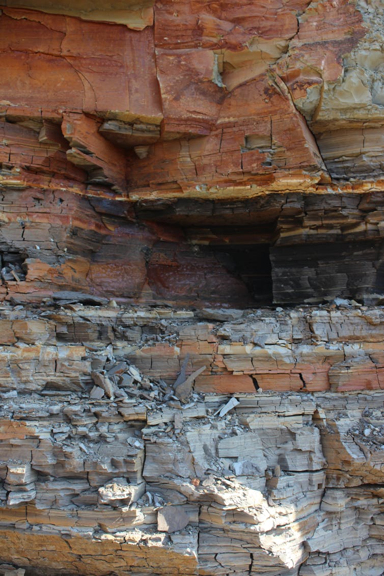 A rock face with several blocky layers of rock, in different stripes of color. The top layers are a darker clay, while the bottom layers are a lighter volcanic ash.
