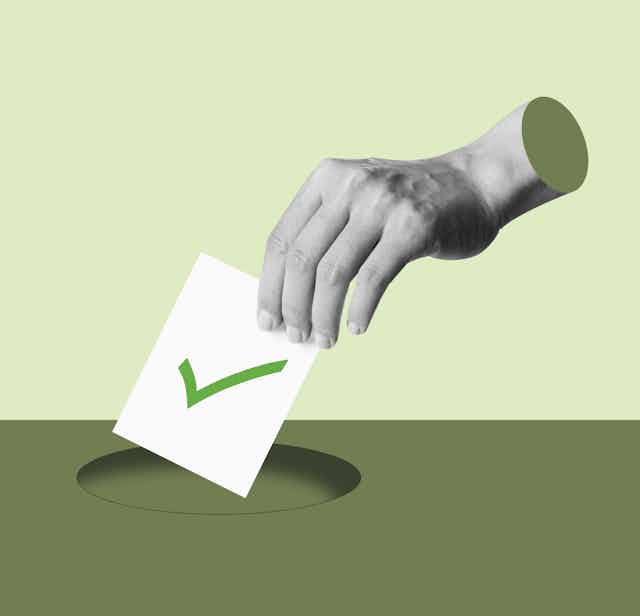 A hand putting a voting ballot with a green tick on it into a hole
