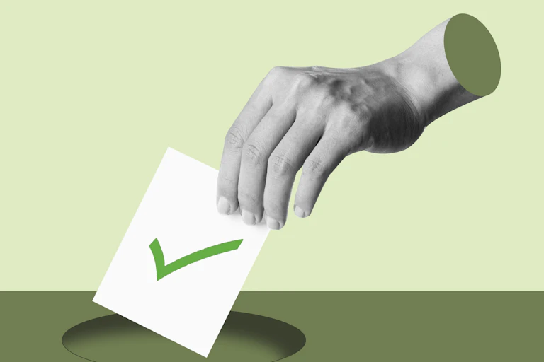 A hand putting a voting ballot with a green tick on it into a hole