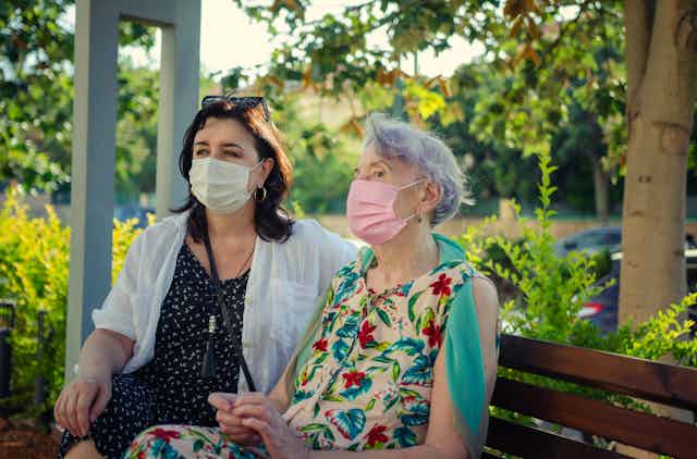 A younger woman and an older woman wearing masks sitting on a bench.