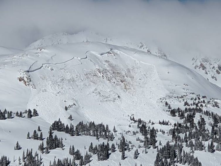 A domed mountain with snow clearly slid down the full width of one side.