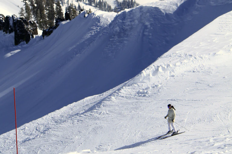 A person stand on skis looking over a sharp drop off at Tahoe Palisades.