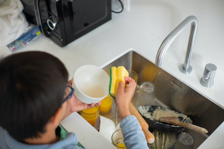 A young boy washes dishes in a sink.