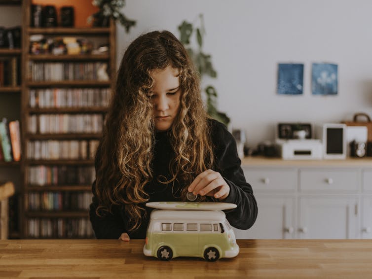 A young girl puts a coin in a money box shaped like a Kombi van.