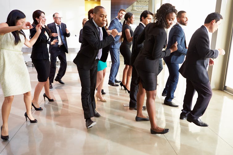 A group of people in office clothes dance in lines.