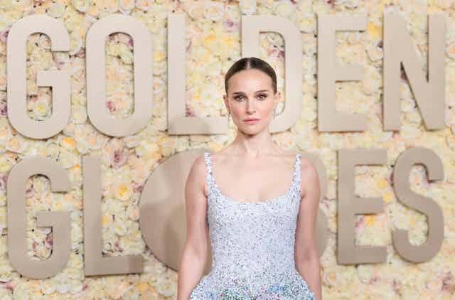 Natalie Portman on a red carpet in an embellished white gown. 