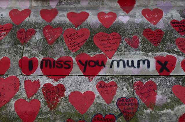 Many red hearts painted on a concrete wall. Short messages are written in the hearts and 'I miss you mum x' is written across several of the hearts in black ink.