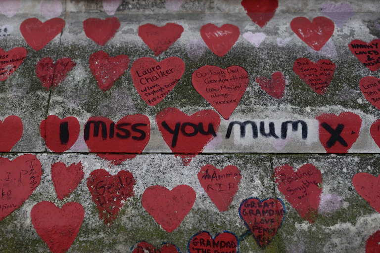 Many red hearts painted on a concrete wall. Short messages are written in the hearts and 'I miss you mum x' is written across several of the hearts in black ink.