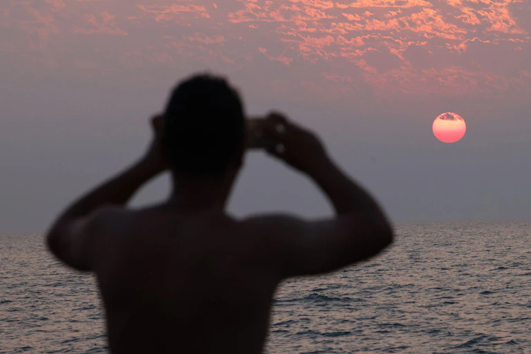 A figure in silhouette photographs the sun rising over a lake.