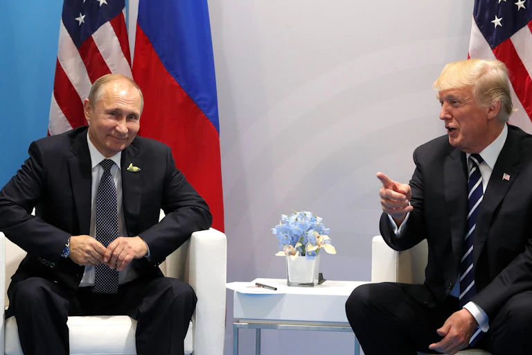 Donald Trump and Vladimir Putin sitting in front of their national flags.
