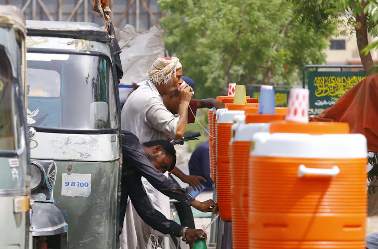 A roadside row of water coolers attended by people leaning out of cars and vans.