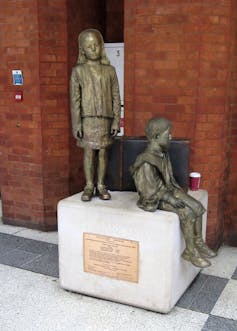 statue of a girl standing and boy sitting down.