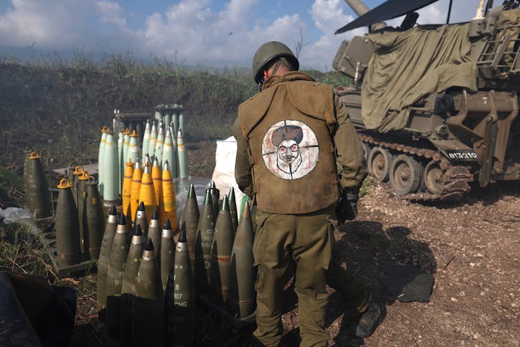 Israeli soldier stacks shells. He is wearing battledress with a picture depicting Lebanese Hezbollah leader Hassan Nasrallah as a target.