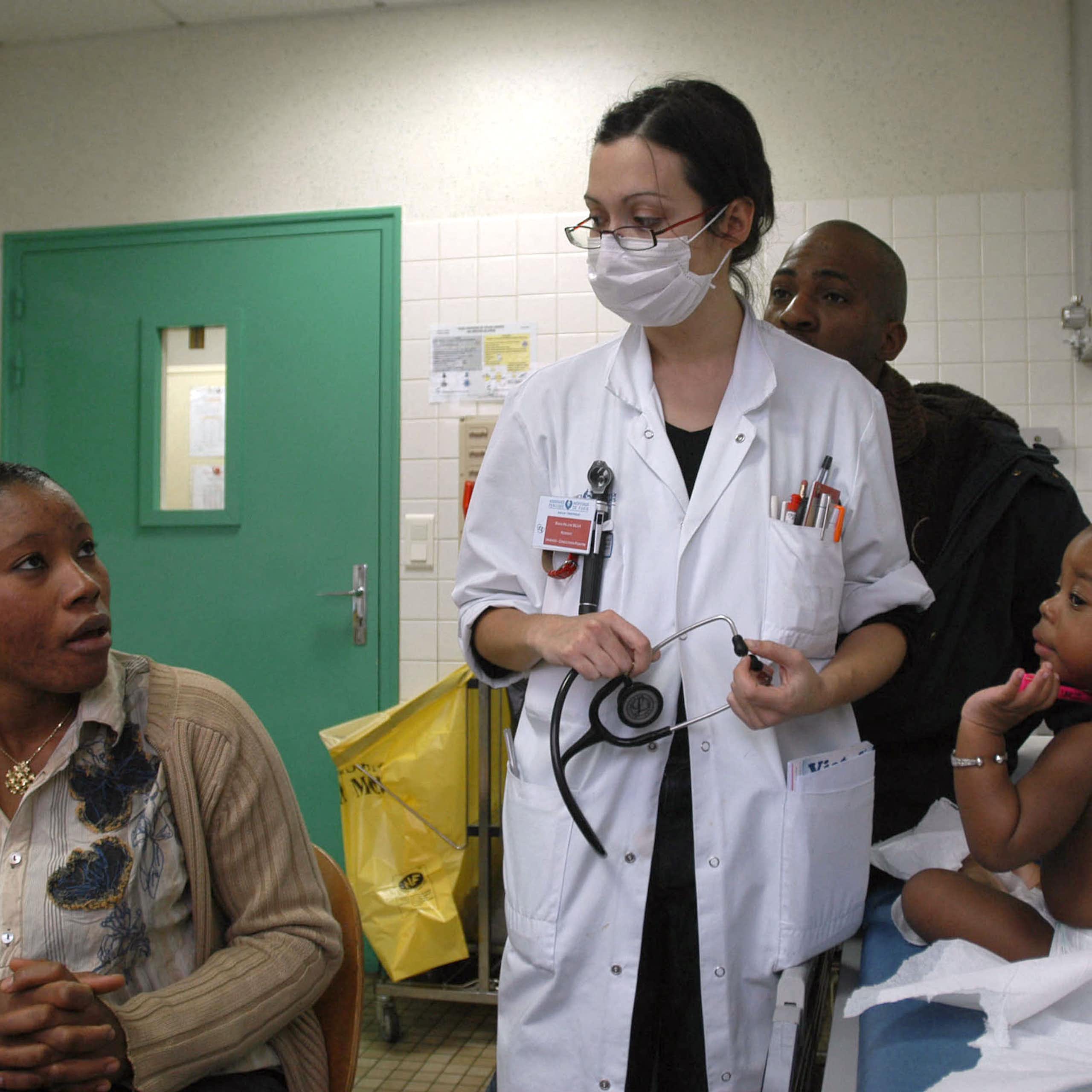 Une professionnelle de santé équipée d'un masque chirurgicale s'occupe d'un jeune enfant malade, en présence de ses parents.