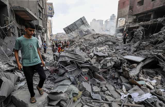 Un joven camina junto a los escombros de un edificio destruido por una bomba.