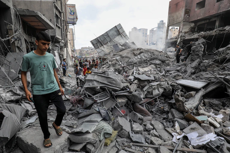 Un joven camina junto a los escombros de un edificio destruido por una bomba.